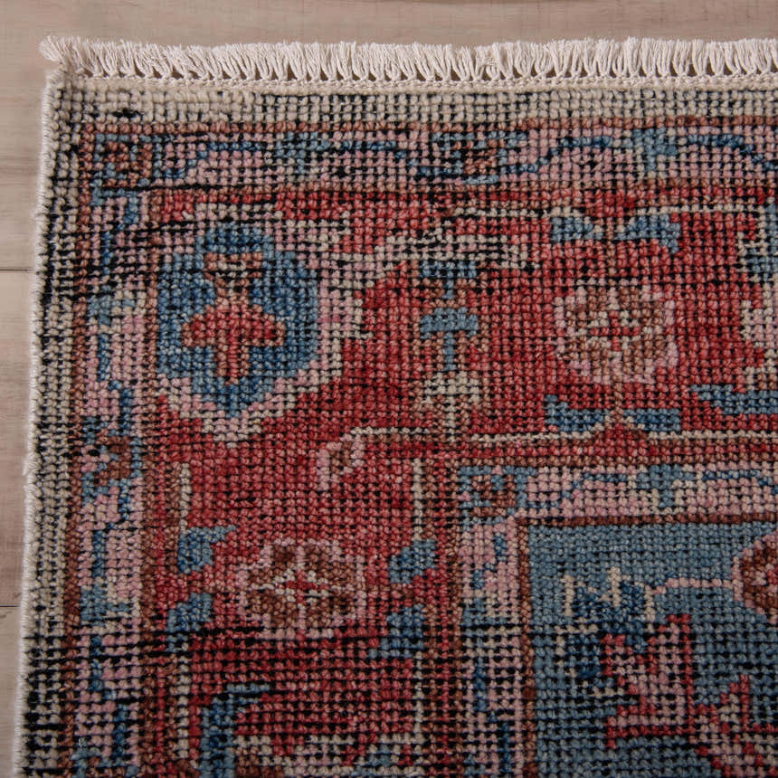 Close up of the hand knotted Rizzy CET723 area rug. Features a traditional design with beige, blue, dark red, and ivory hues. Corner