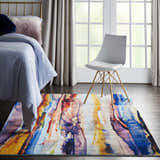 Bedroom scene with a Nourison Le Reve Multicolor rug, gold bed frame, and white chair near a window.