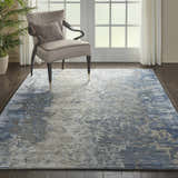 Living room scene with a Nourison Prismatic Denim rug, gray chair, dark wood floors, and natural light.