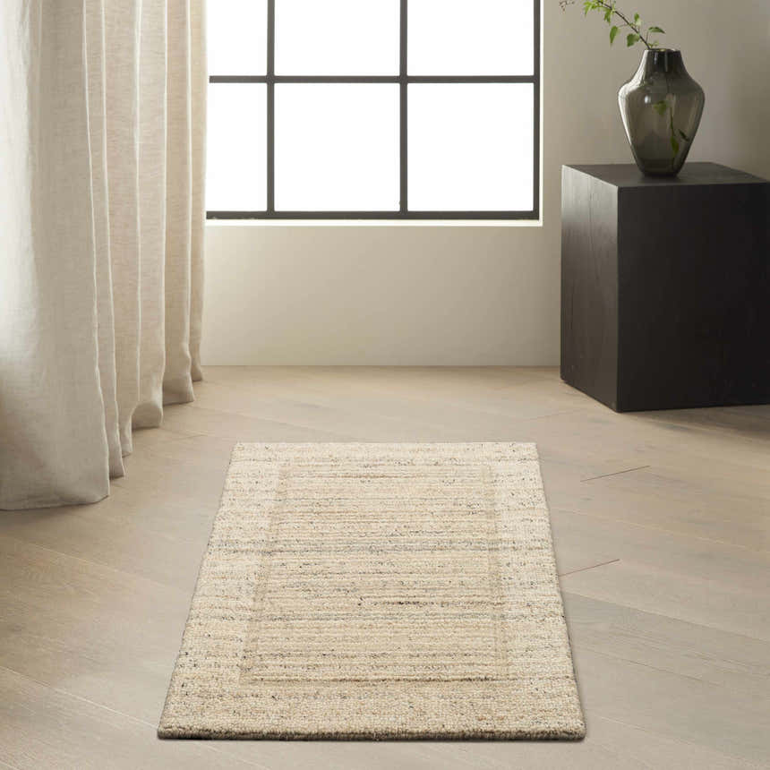 Minimalist room scene with a Calvin Klein CK082 Ridge beige ivory farmhouse rug on light wood floors. Neutral drapes and black accents.