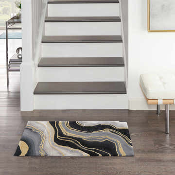 Entryway scene with Nourison Prismatic Charcoal Grey rug, white stairs, wood floors, and modern white bench.