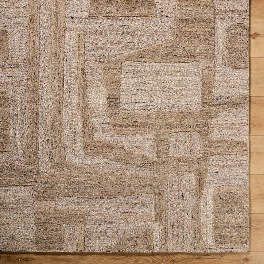 Close-up of the Brasen Tan Area Rug showing its beige, tan, and taupe geometric pattern and hand-tufted wool texture. Corner