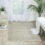 Bright room featuring Nourison Starlight Sea Mist rug, white bench with throw, and green plants. Modern, airy style.