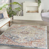 Living room scene with a Nourison Soraya Blue Multicolor rug, white sofa, fireplace, and gray chair.