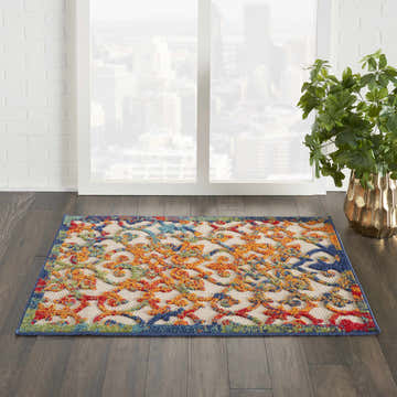 Modern room featuring Nourison Aloha Multicolor Outdoor Area Rug with blue trim and orange, red, green, and blue floral pattern.