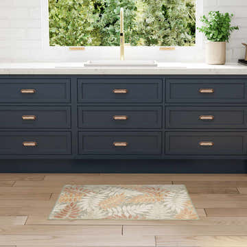 Kitchen scene with a Nourison Aloha Sage Rose rug, navy cabinets, and light wood floors.