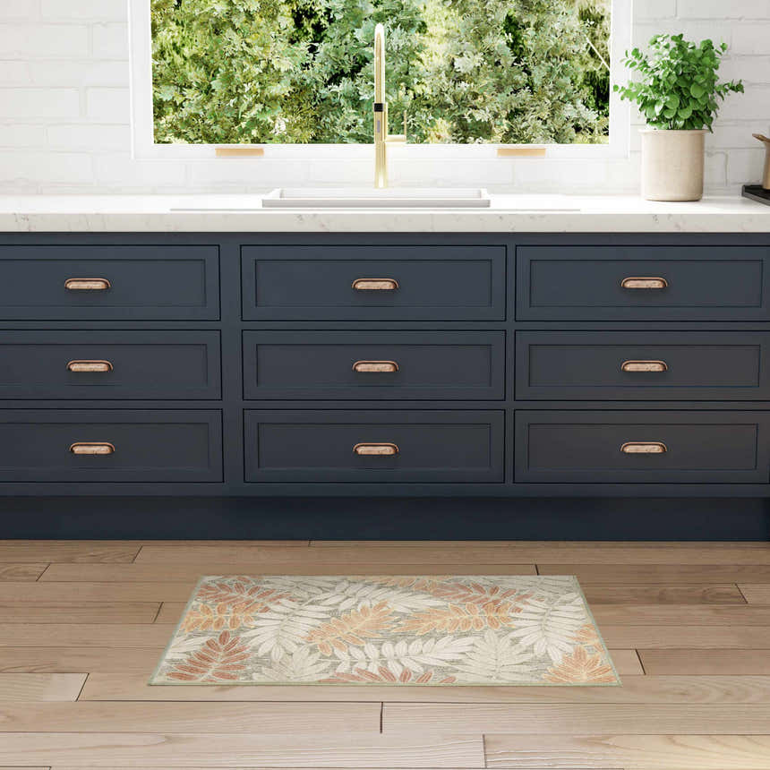 Kitchen scene with a Nourison Aloha Sage Rose rug, navy cabinets, and light wood floors.