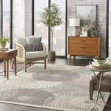 Mid-century modern living room with a Nourison Graphic Illusions grey rug, rattan chair, and wood dresser.