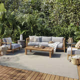 Outdoor patio scene with gray furniture and a Nourison Courtyard Ivory Silver rug on a wood deck surrounded by lush greenery.
