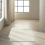 Minimalist room scene with ivory Calvin Klein Pretoria rug on light wood floor. Neutral tones, natural light.