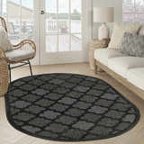 Living room scene with an oval Nourison Easy Care Charcoal Black rug, wicker chair, and neutral sofa.