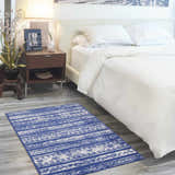 Bedroom scene with Nourison Whimsicle Navy Ivory rug, white bedding, wood nightstand, and soft, inviting ambiance.