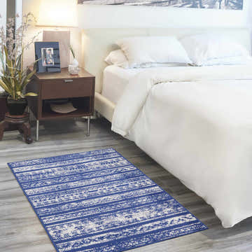 Bedroom scene with Nourison Whimsicle Navy Ivory rug, white bedding, wood nightstand, and soft, inviting ambiance.