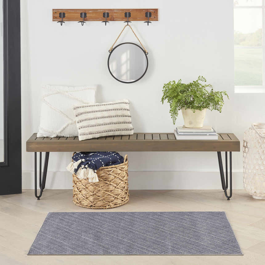 Entryway scene with a grey Nourison washable rug, wood bench, pillows, mirror, and plant. Modern style.