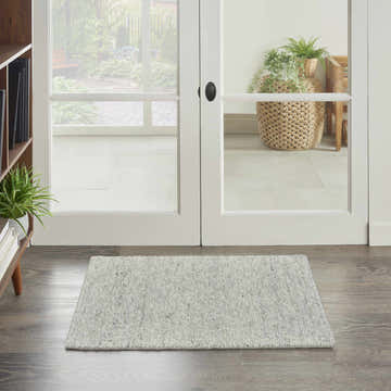Entryway with silver gray Nourison Alanna Farmhouse rug on wood floor, white doors to garden, and bookshelf.