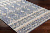 Close-up of the Eben Area Carpet. Hand woven cotton rug in light blue with an off-white geometric pattern. Corner