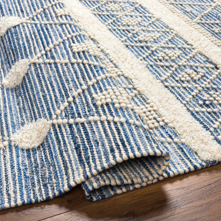 Close-up of the Eben Area Carpet showing its blue and off-white woven texture and geometric, tufted details. Fold