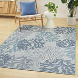 Coastal living room scene with a Nourison Garden Oasis Blue Area Rug, light wood floors, and a woven chair.