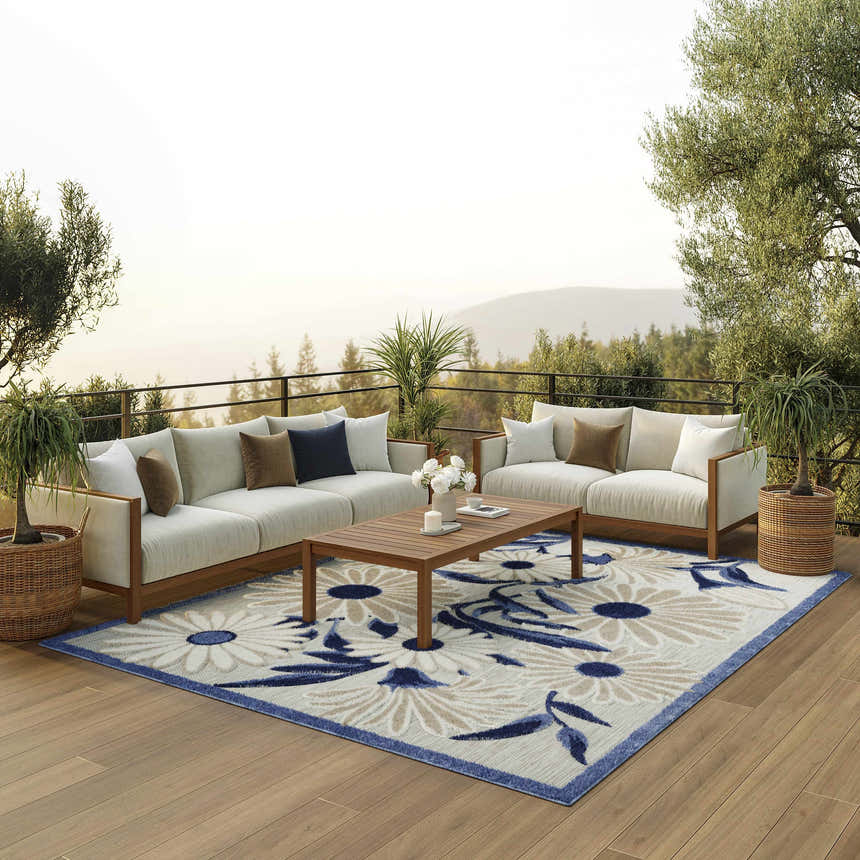 Outdoor patio scene with sofas, wood table, and Nourison Aloha Blue Grey Outdoor Area Rug with floral pattern.