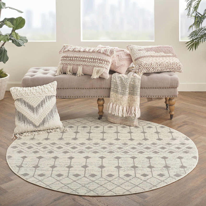 Cozy sunroom with a round Nourison Grafix Ivory/Grey Bohemian rug, tufted bench, and textured throw pillows.