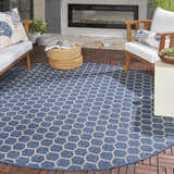 Outdoor patio scene with a round Nourison Twist Blue rug, wood furniture, and a modern fireplace.