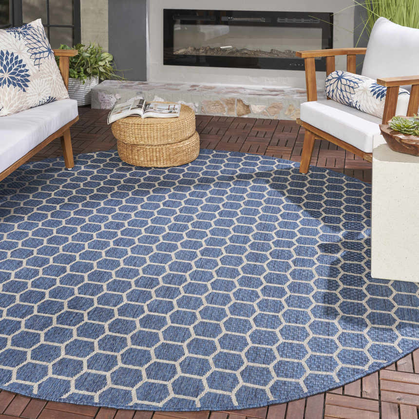 Outdoor patio scene with a round Nourison Twist Blue rug, wood furniture, and a modern fireplace.
