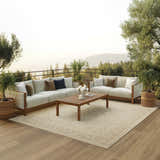 Outdoor patio scene with cream sofas, wood table, and Nourison Tulum Cream Outdoor Area Rug.