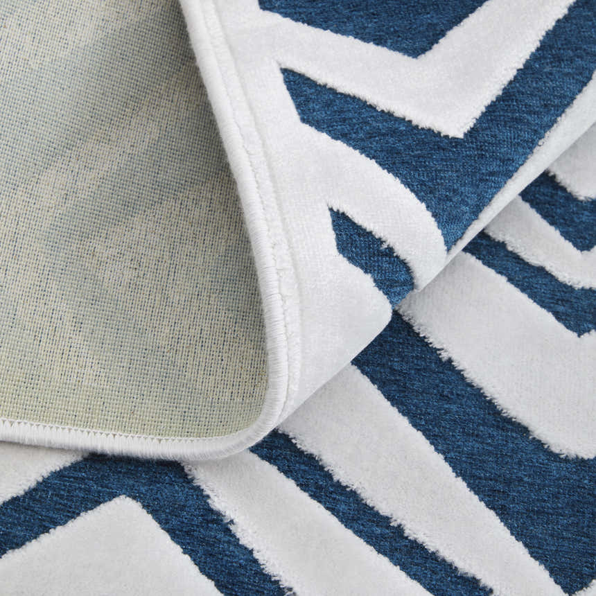 Close-up of Feizy Saphir Mira rug showing blue and white diamond pattern, texture, and cotton backing. Fold