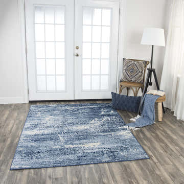 Living room scene with Rizzy EN7262 area rug in blue and ivory, styled with a chair, stool, and throw blanket. Roomscene-Rectangle