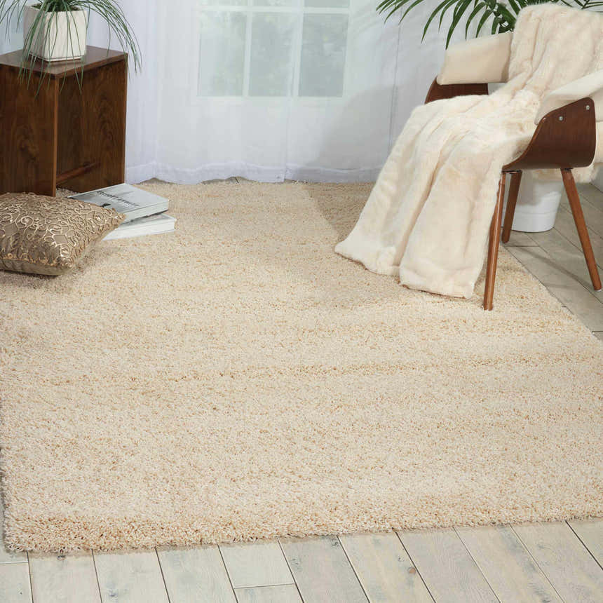 Cozy room scene with a cream Nourison Amore shag rug, wood chair with throw, and wood side table.