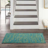 Entryway scene with a Nourison Essentials Blue Green Outdoor Area Rug on dark wood floors.