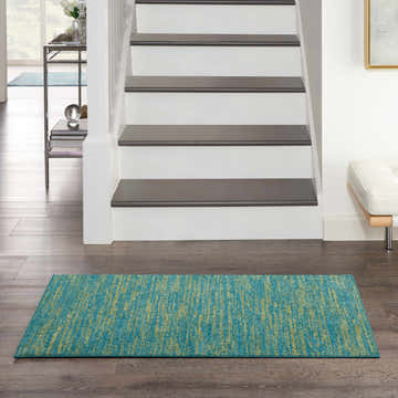 Entryway scene with a Nourison Essentials Blue Green Outdoor Area Rug on dark wood floors.