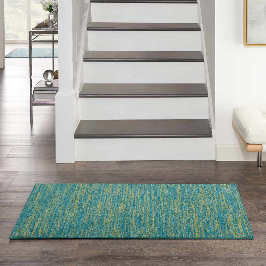 Entryway scene with a Nourison Essentials Blue Green Outdoor Area Rug on dark wood floors.