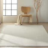 Minimalist room scene with Calvin Klein Pretoria Ivory rug, wood chair, blanket, and tree branch decor.