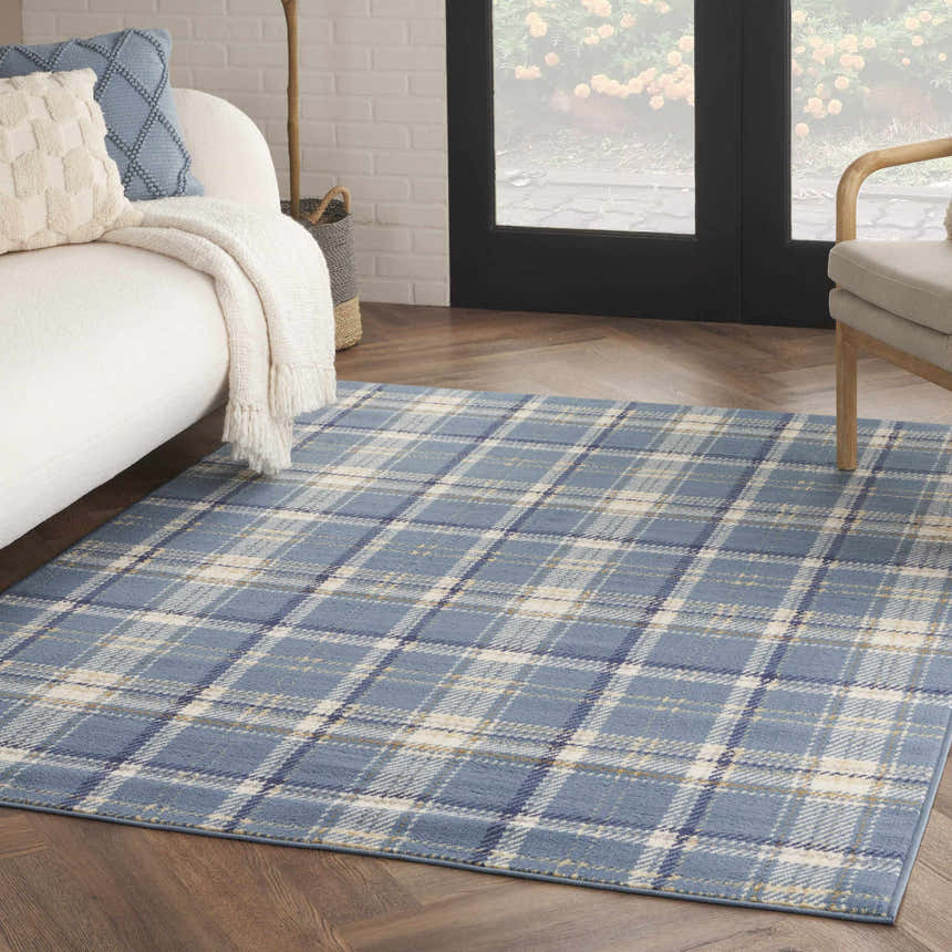 Living room scene with a light blue plaid Nourison Grafix area rug, white sofa, and wood floors.