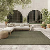Olive Nourison Tulum outdoor rug on a stone patio with a neutral sectional sofa and potted plants.