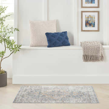 Light-filled room with a Nourison Astra Denim Multicolor vintage rug, pillows, throw, and potted tree.
