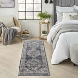 Bedroom scene with Nourison American Manor Blue Farmhouse rug, wood floors, rattan chair, and bed with gray accents.