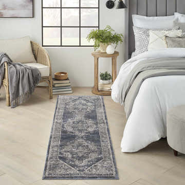 Bedroom scene with Nourison American Manor Blue Farmhouse rug, wood floors, rattan chair, and bed with gray accents.