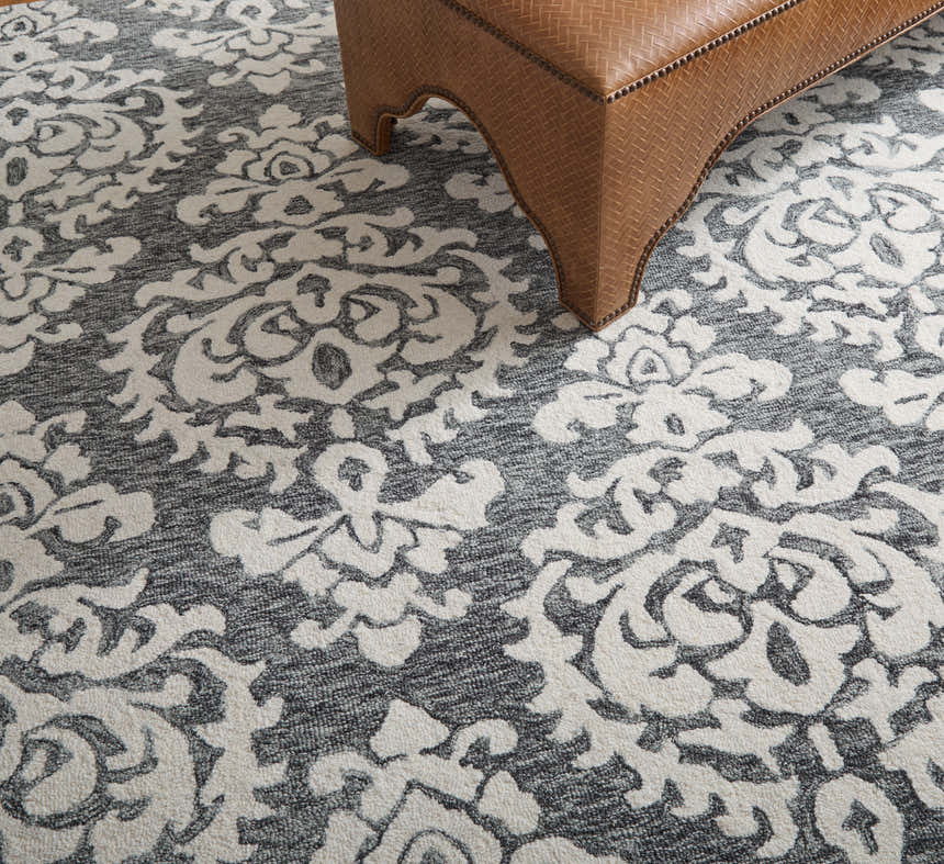 Close-up of Feizy Belfort Traditional Floral rug in gray, ivory, and black with a brown leather ottoman. Roomscene-Rectangle