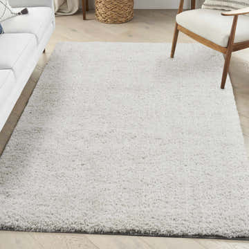 Living room scene with a Nourison Modern Shag Silver rug, white sofa, and wood accent chair on light wood floors.