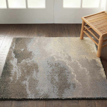 Living room scene with the Nourison Twilight Storm rug in storm color, wood floors, and a bamboo stool.