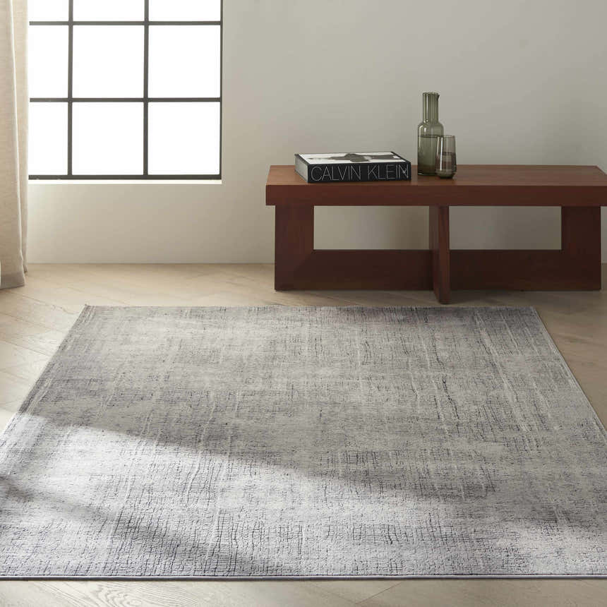 Minimalist room with Calvin Klein CK970 Vapor Grey Ivory rug, wood bench, and herringbone floors. Modern style.