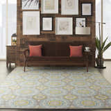 Living room scene with a Waverly Sun N' Shade Jade rug, brown sofa, wood wall, and botanical art. Coastal style.