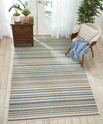 Entryway with Barclay Butera Lido Blue Cream rug, wood floors, side table with plants, and chair with blue throw.