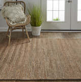 Entryway with jute Feizy Kaelani rug, woven geometric pattern, brown wood floor, rattan chair, and neutral pillow. Roomscene-Rectangle