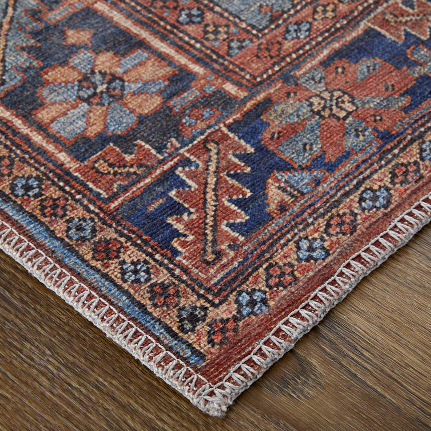 Close-up of Feizy Rawlins rug. Red, tan, and blue geometric medallion pattern with intricate details and stitched edge. Corner