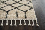 Close up of Nourison Moroccan Shag Cream Tribal rug, showing shag texture, diamond pattern, and fringe on dark wood floor.