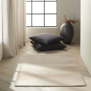 Minimalist room scene with Calvin Klein Home Luster Wash Ivory rug, gray cushions, black vase, and light wood floors.