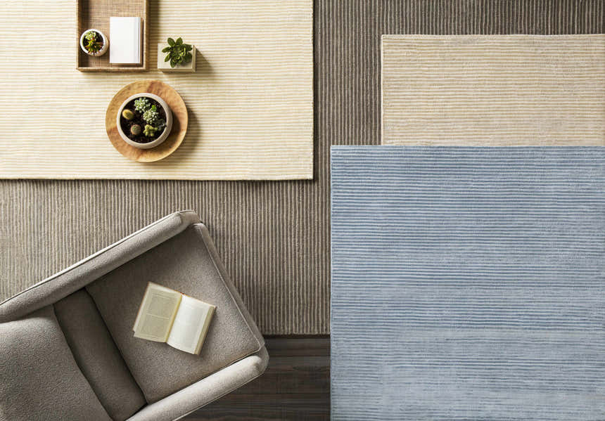 Overhead shot of Ahmeek Area Rugs in gray, beige, and blue with subtle horizontal stripes. Armchair and plants included. Styleshot